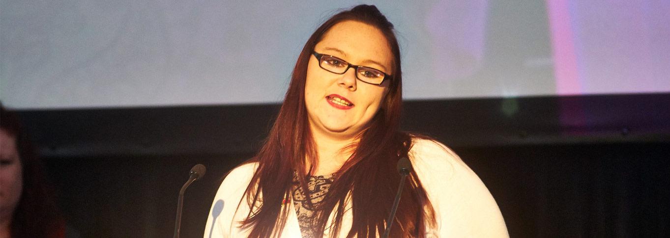 Becky, who has long brown hair and glasses, speaking at an event. 