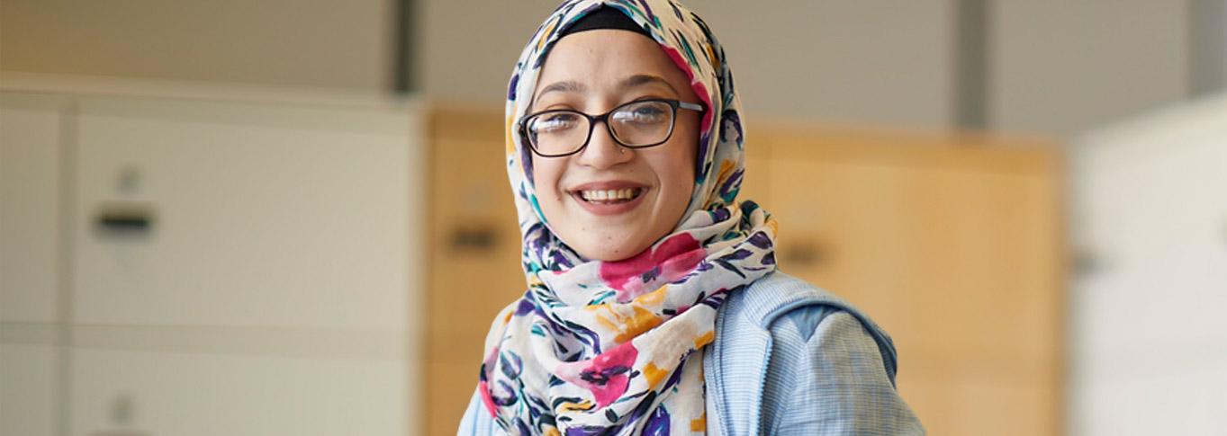 Sema, who wearing glasses and a head scarf, smiling. 
