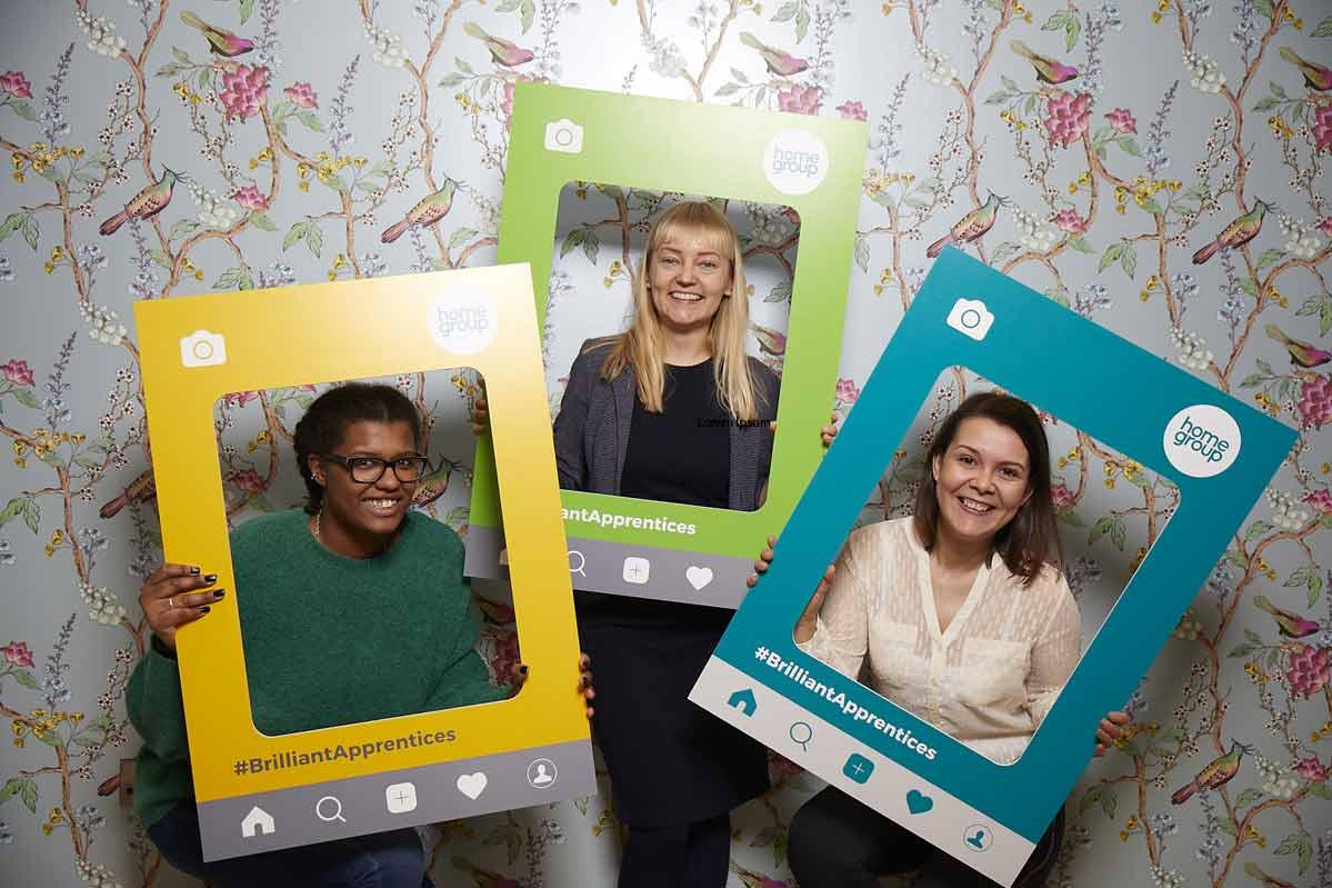 Three of our apprentices hold picture frames and smiling.