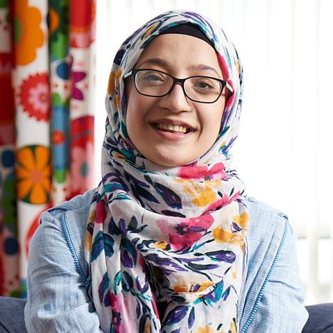 Sema who wears glasses and a head scarf, smiling. 
