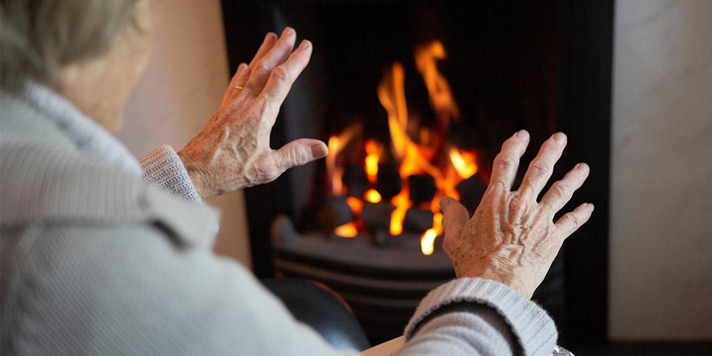 An older person warming their hands in front of a fireplace.